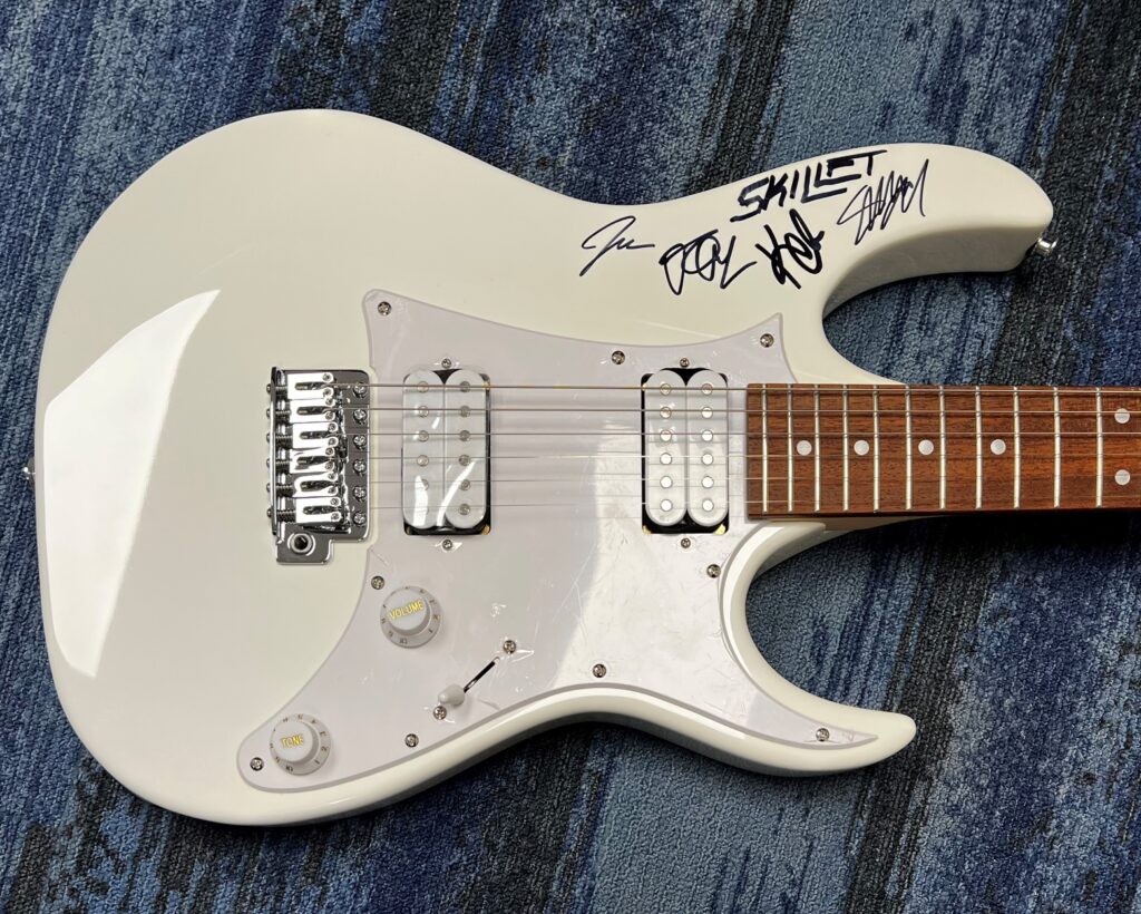 A creme colored guitar signed by the members of Skillet